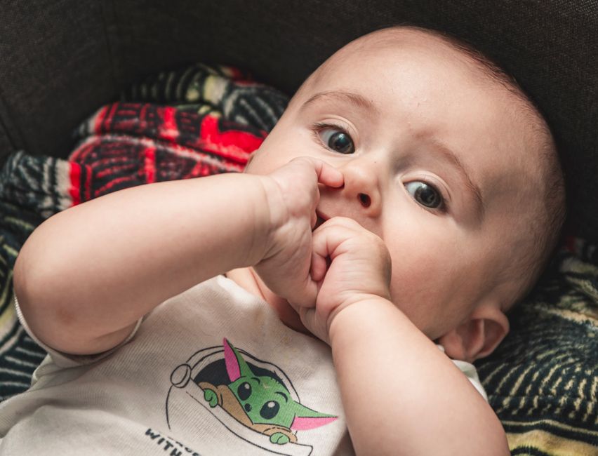 A baby nibbling their fingers during teething in a safe nursery setting