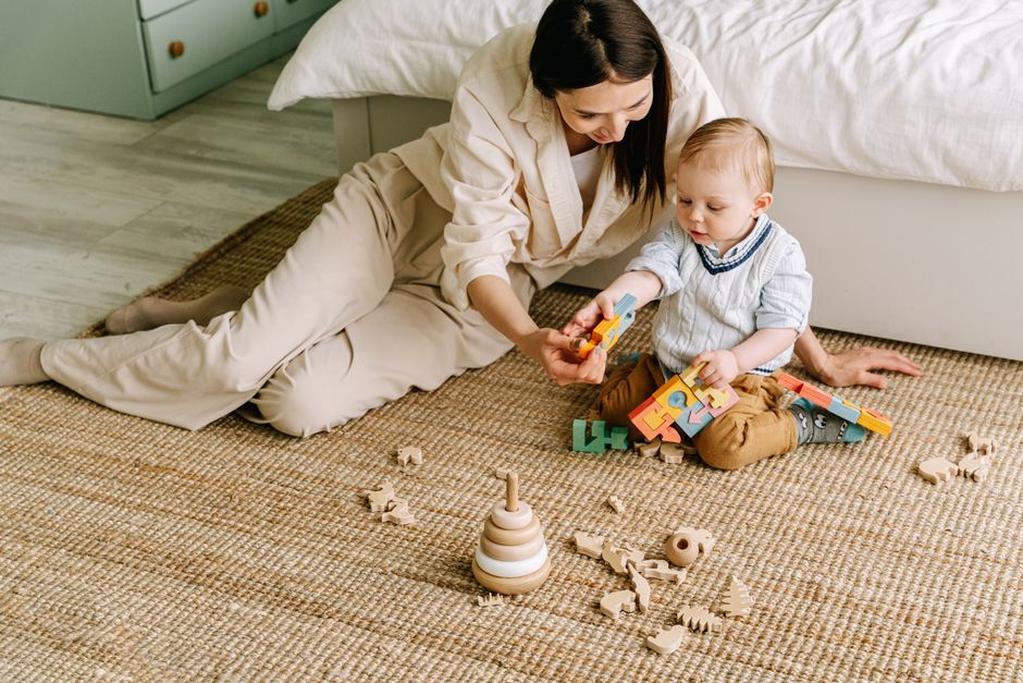 Mother and baby engaging in play with wooden toys on a cozy mat