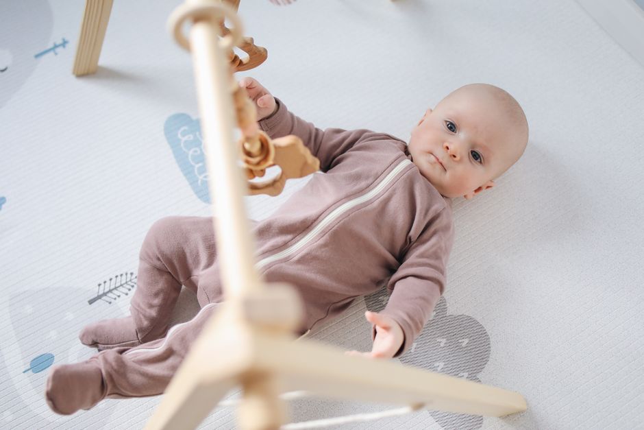Cute baby in a cozy onesie playing with wooden toys on a soft mat
