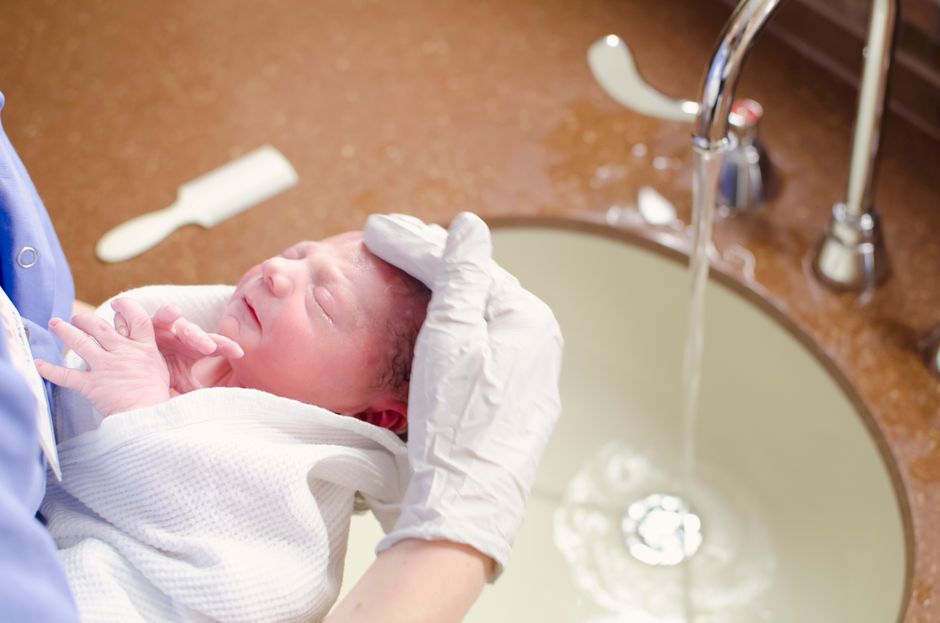 A woman gently supports an infant in a water-filled tub during a bath