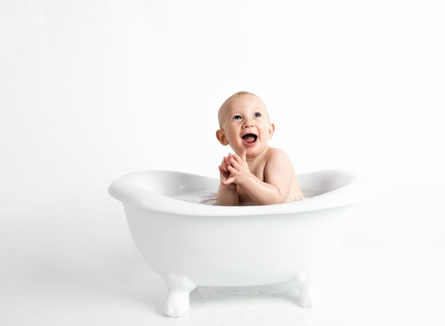 Cute baby laughing and clapping in a white bathtub against a white background