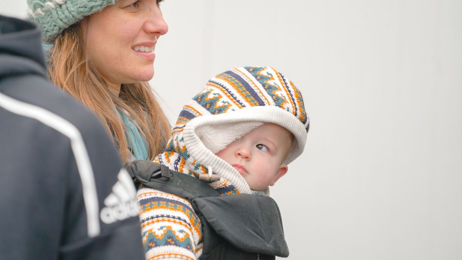 A mother carrying her baby in a cozy winter outfit outdoors in an ergonomic baby carrier