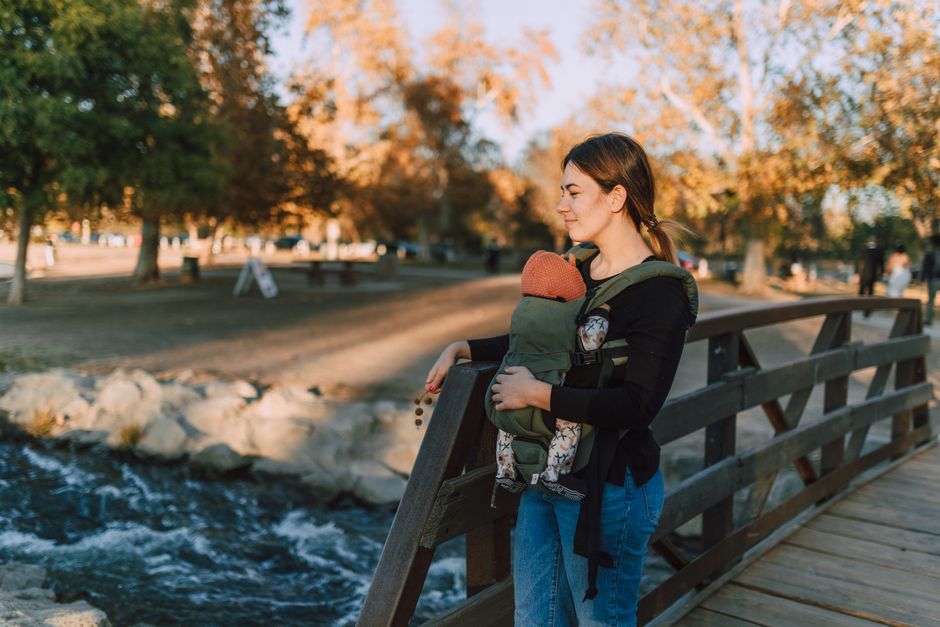 A mother carrying her baby on a wooden bridge in an autumn park