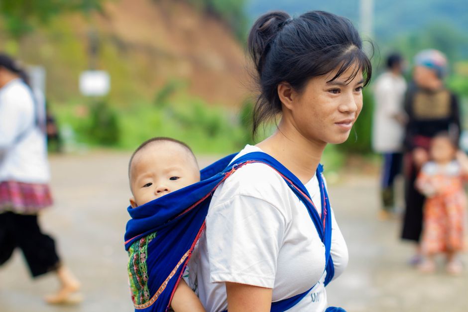 A mother wearing an ergonomic baby sling wrap outdoors