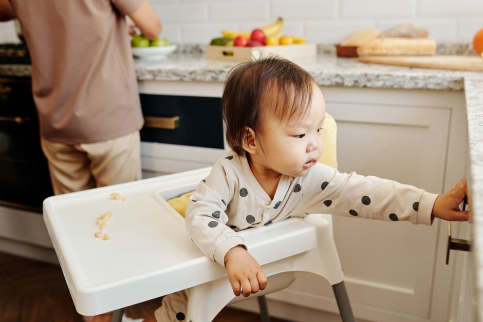 A toddler seated in a high chair reaching for healthy, safe food