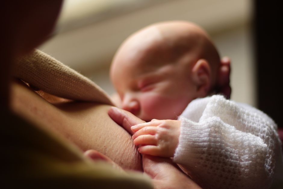 Mother holding and soothing baby while feeding in a cozy nursery