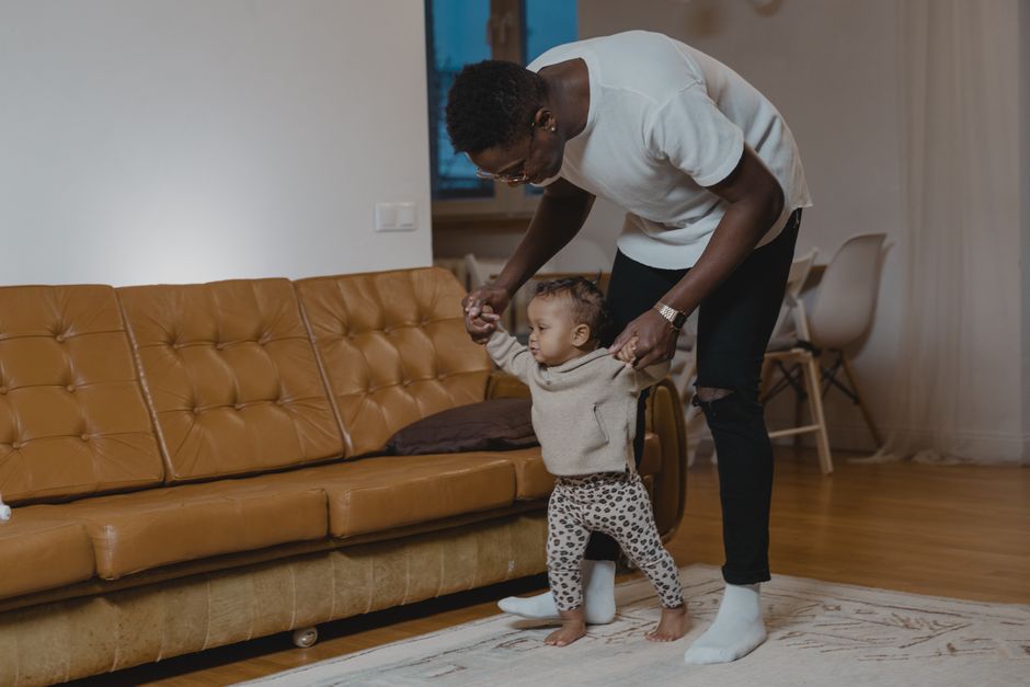 A parent helping a happy baby practice balance and first steps in the living room