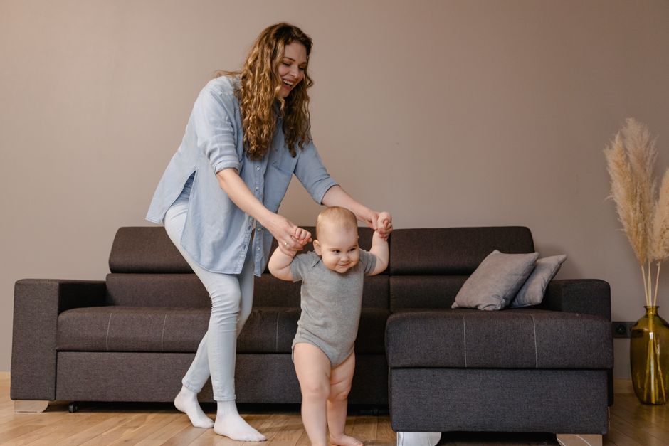 A joyful moment of a mother guiding her baby as they play together indoors.