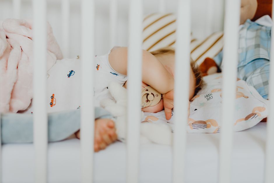 A baby peacefully sleeping with a pacifier in a cozy crib with plush blankets