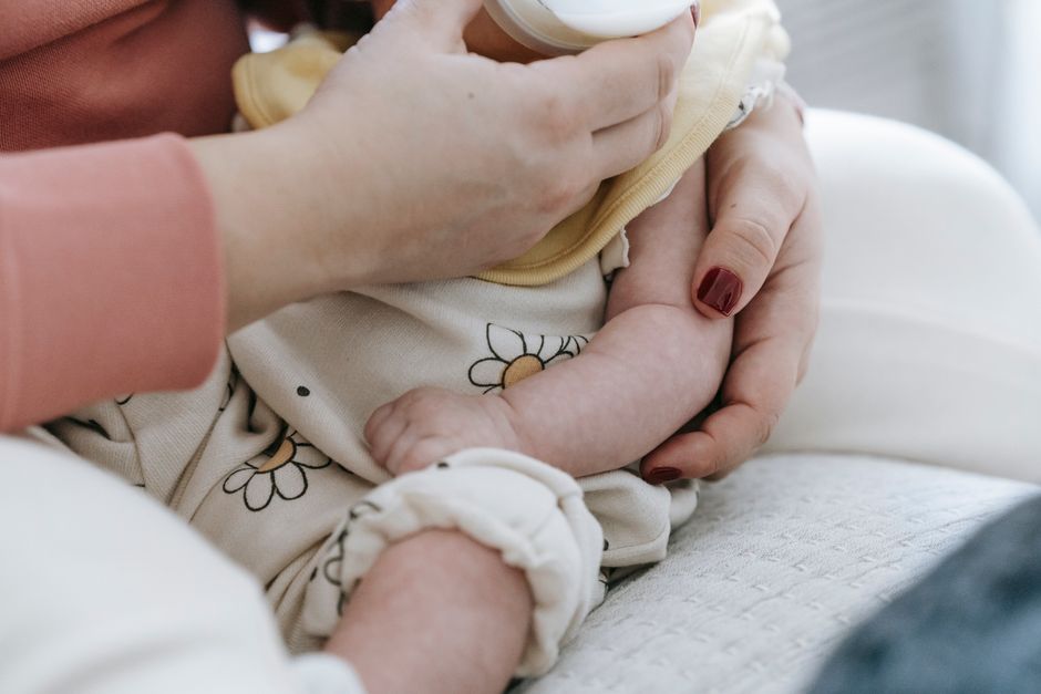 Anonymous mother embracing and feeding newborn baby with milk at home