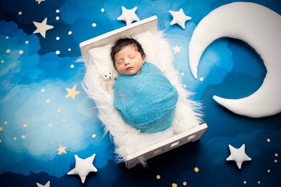 A cute newborn baby wrapped in blue sleeping in a crib with star and moon decor