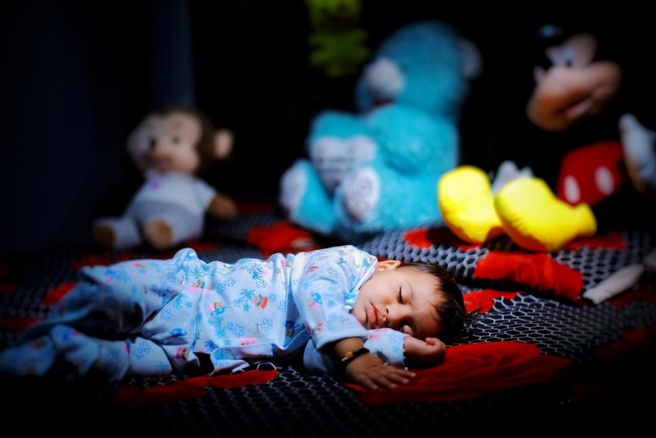A serene baby boy in pajamas sleeping peacefully amidst colorful stuffed toys in a cozy bedroom setting