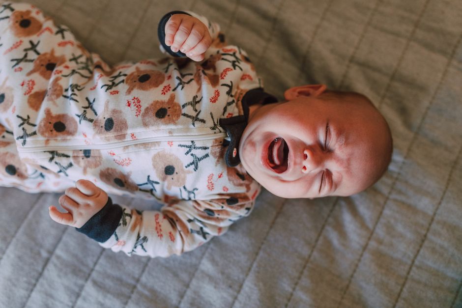 A crying infant on a bed overwhelmed by overtiredness