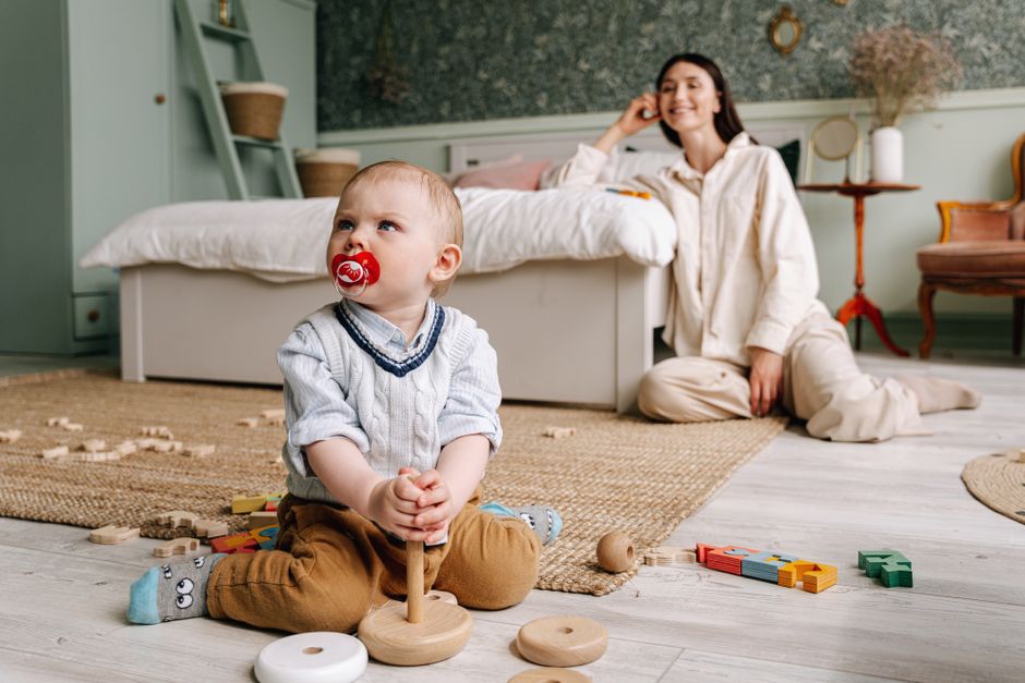 A mother and child playing together with open-ended wooden toys on a soft rug