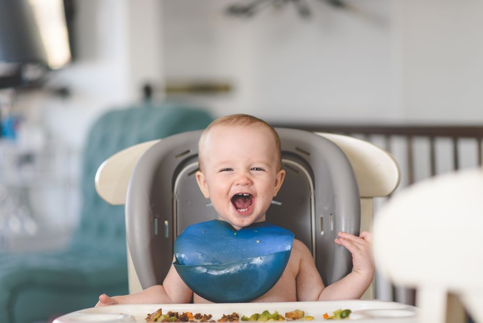 Happy infant sitting in a high chair exploring freshly prepared solid foods during mealtime