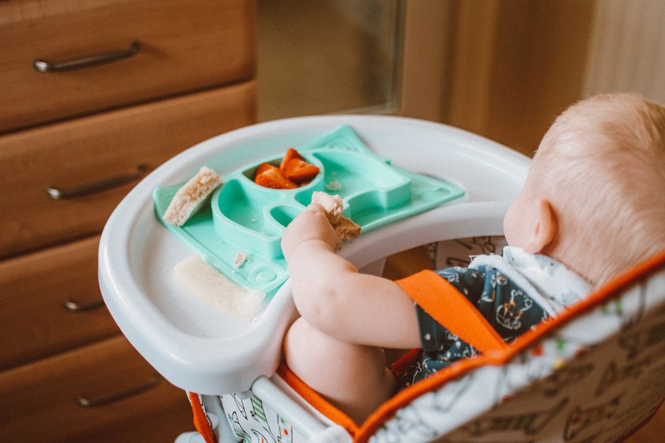 Cute baby enjoying snacks in a high chair with feeding tray