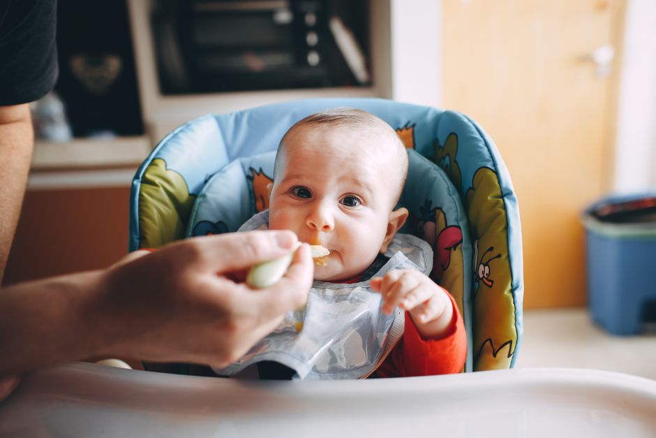 Parent feeding infant baby nutritious food in high chair