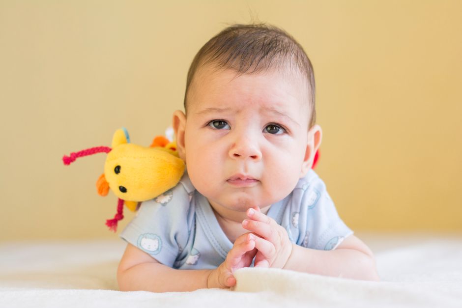 A happy baby practicing gentle, supported tummy time on a soft play mat with high-contrast toys