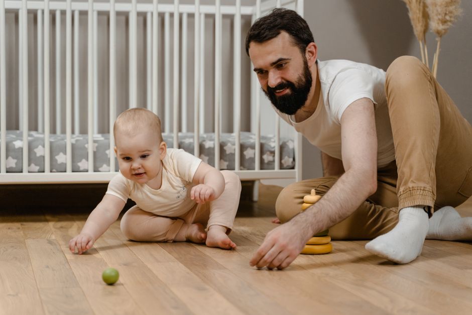 A happy baby girl smiles and plays with a small rubber toy on the floor during developmental tummy time