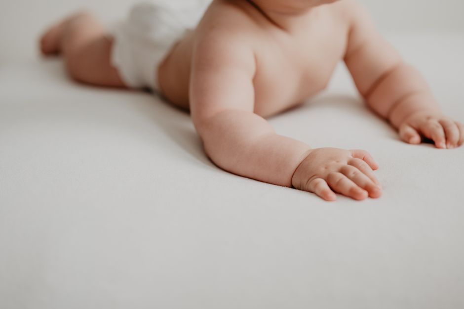 Close-up of a baby in a diaper crawling on a soft, white surface indoors