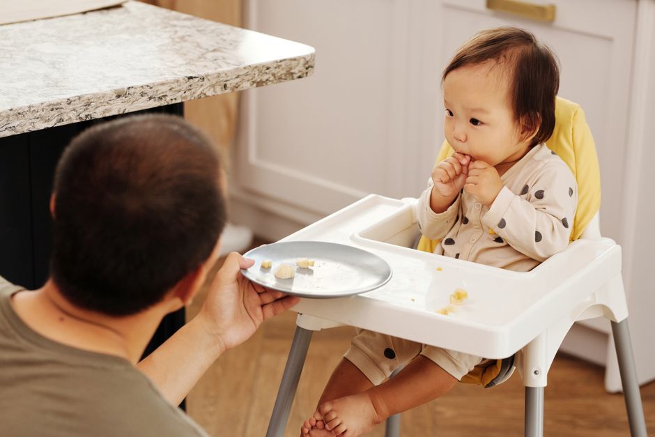 An infant sits in a high chair indoors with a toy