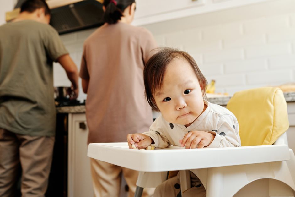 A cute toddler sitting in a high chair eating outdoors