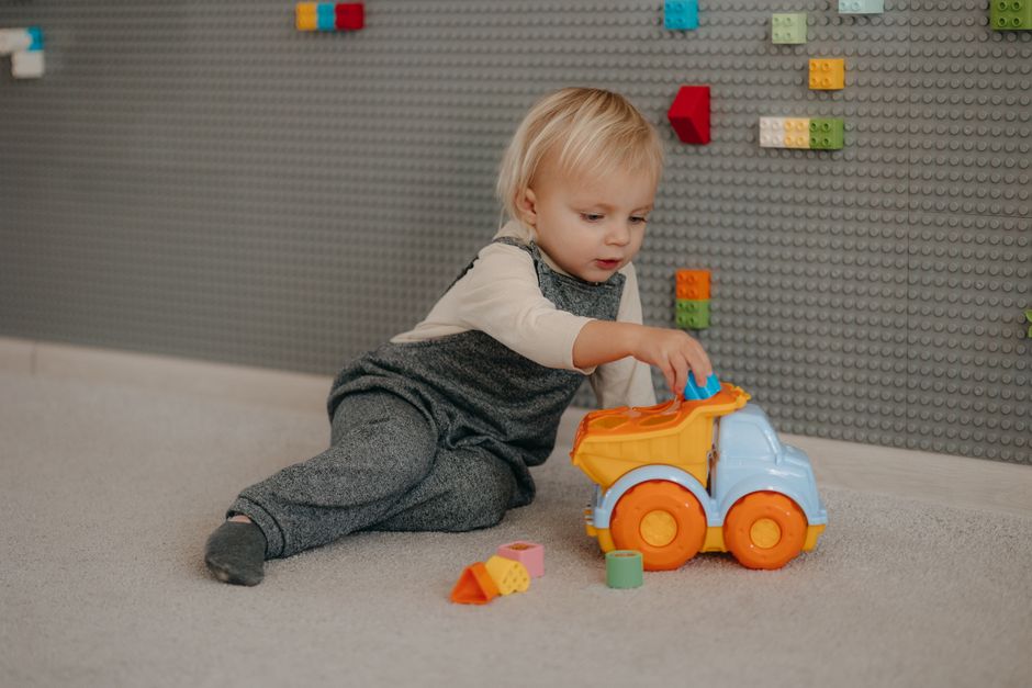 Toddler playing happily with building blocks and toy trucks on floor