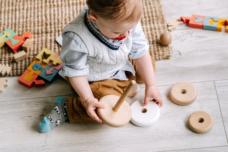 Toddler sitting comfortably on a play mat with wooden toys