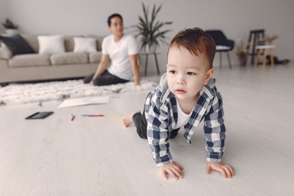 Cute baby boy crawling on the floor while dad watches in a cozy living room setting