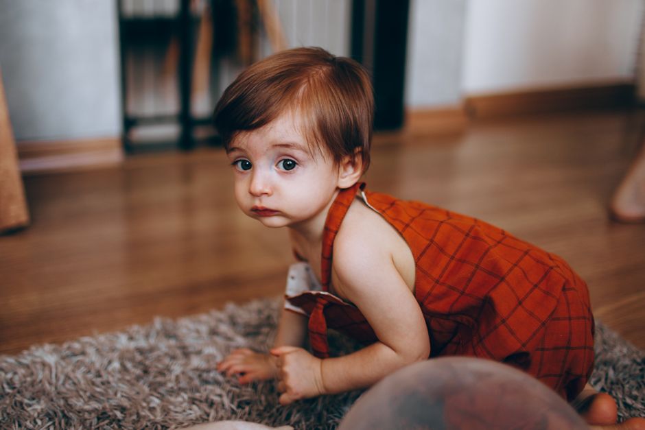 Cute toddler in red outfit crawling on a carpeted floor indoors, exploring the room