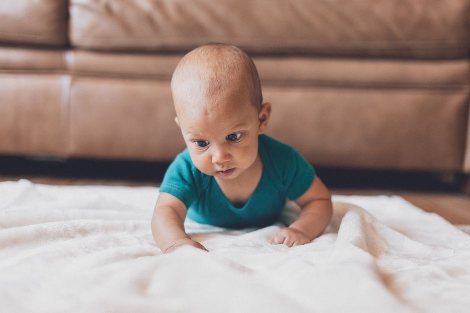 Cute baby crawling on a soft white blanket indoors, showcasing innocence and playfulness