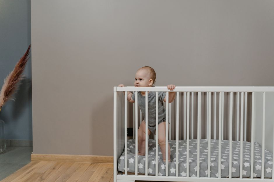 An active infant standing in a wooden crib reaching upwards