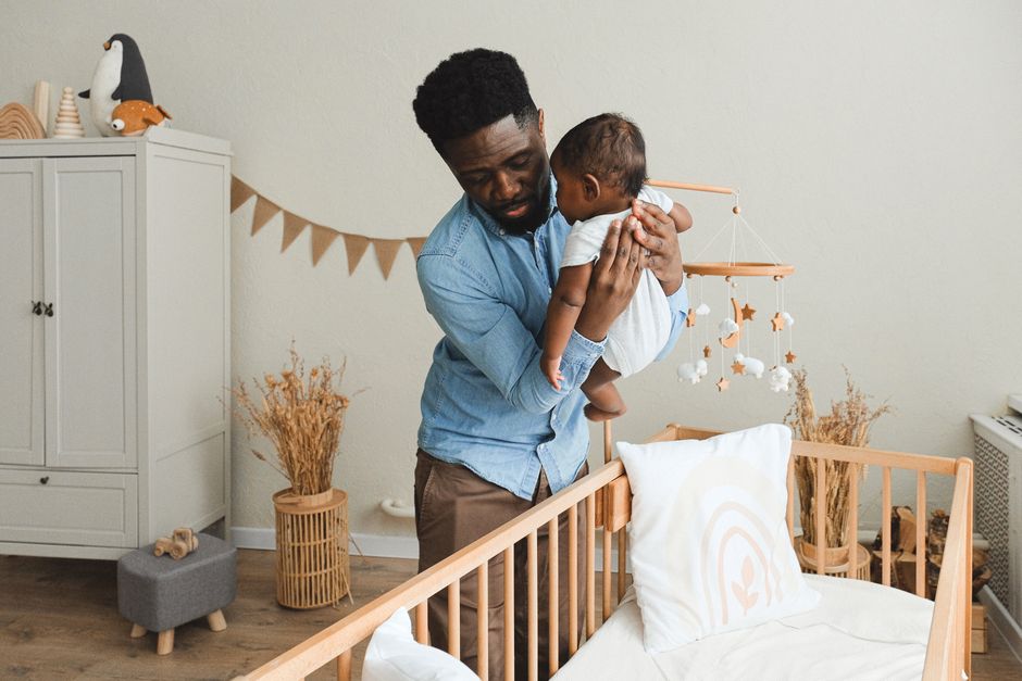 A parent gently placing their sleeping infant into a safe crib