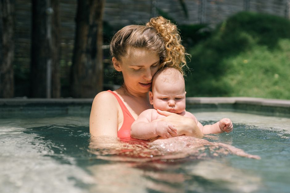 A loving mother holds her baby in a swimming pool, sharing a tender outdoors moment
