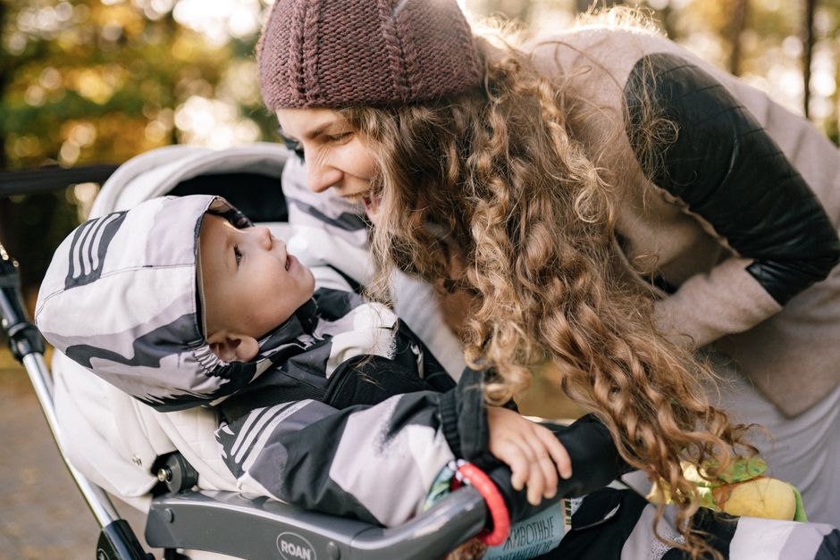 Mother engaging with her baby in a stroller during a sunny day walk