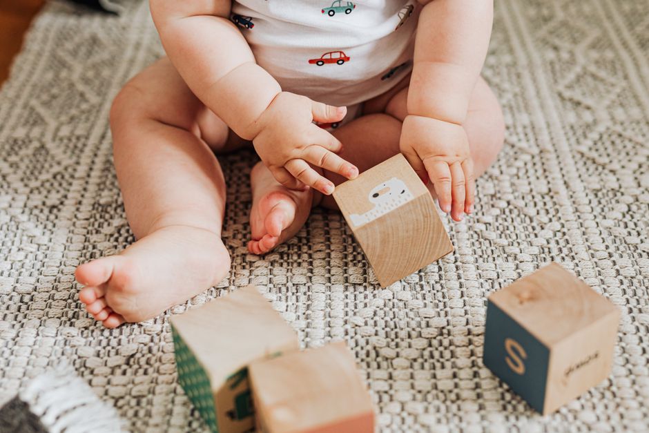 A baby sitting independently and playing with wooden blocks