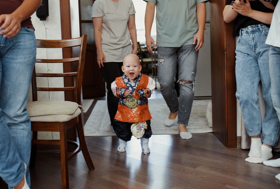 A joyful baby in traditional attire takes first steps with family support