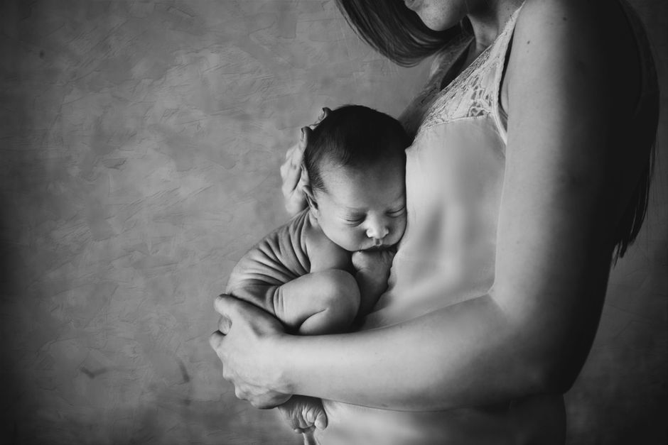 Mother holding sleeping newborn close in black and white
