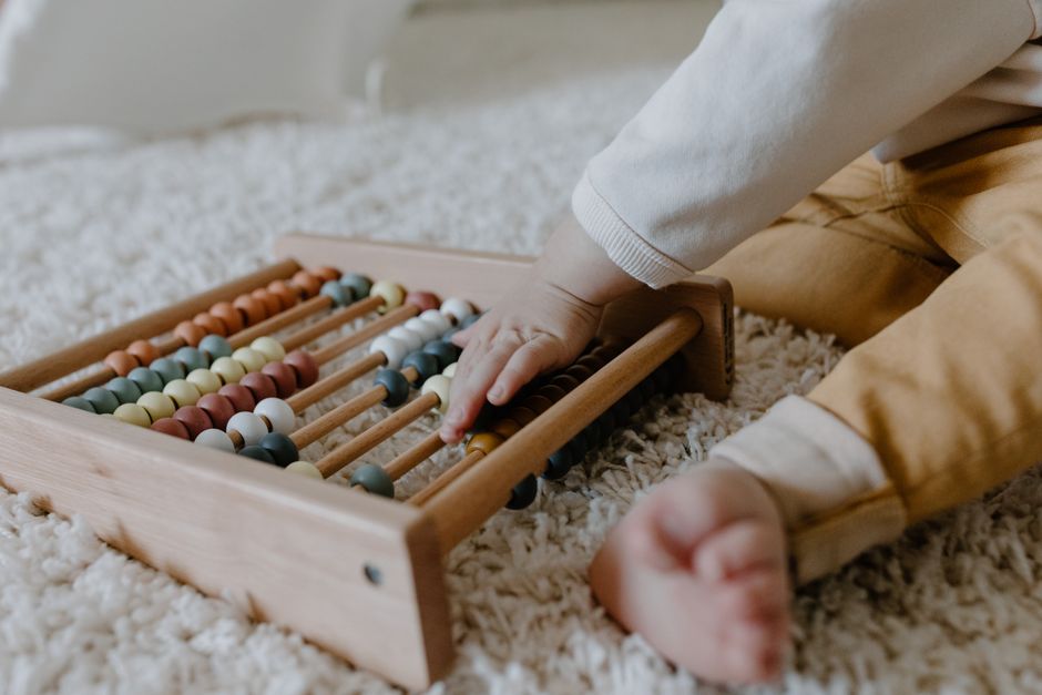 Toddler engaging with a wooden abacus on a fluffy carpet, promoting early learning