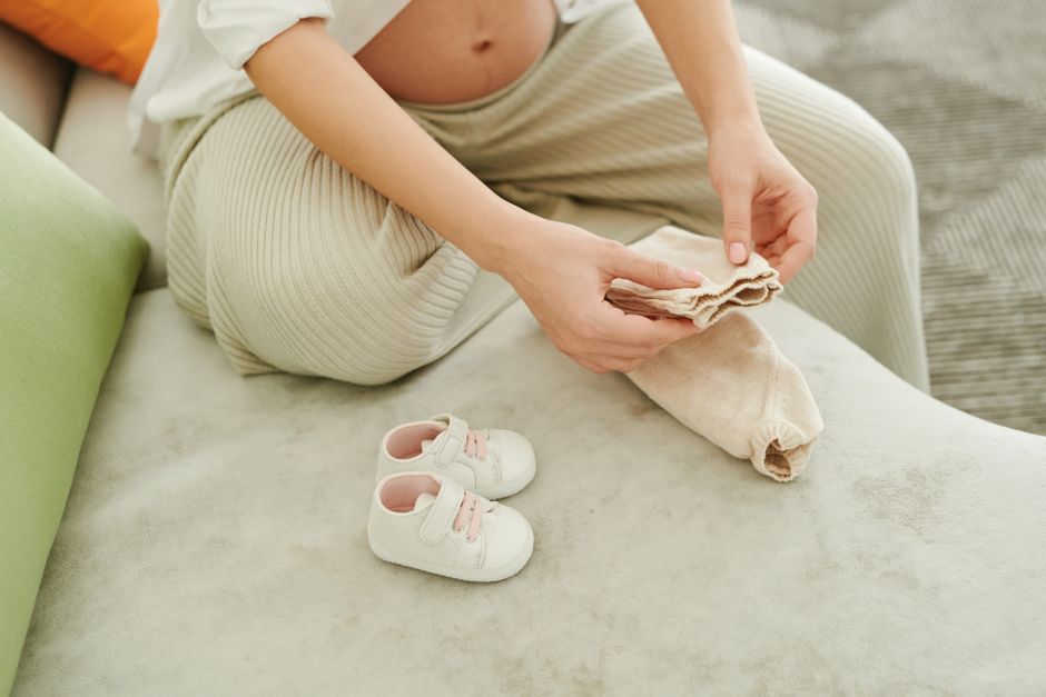 Expecting mother carefully organizing minimalist newborn clothes on sofa