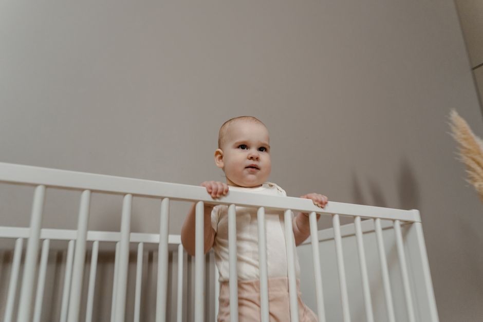 Charming baby standing in a white crib indoors holding the railing
