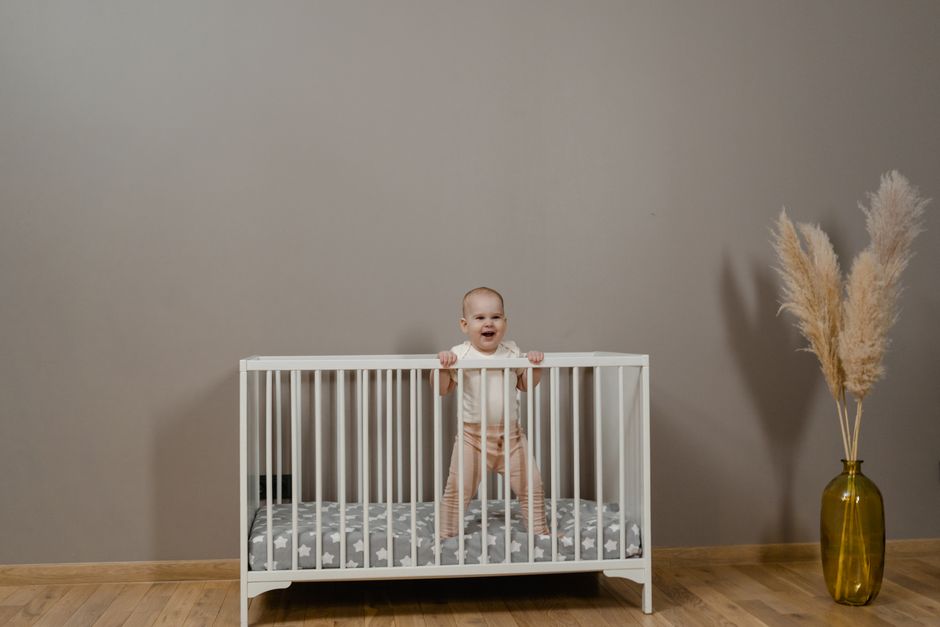Adorable baby smiling in a white crib next to nursery decor
