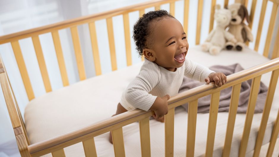 Joyful baby laughing while standing in a wooden crib indoors