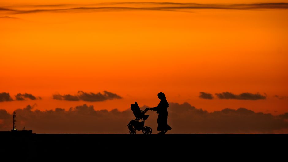 Mother strolling along the waterfront in gentle sunset light