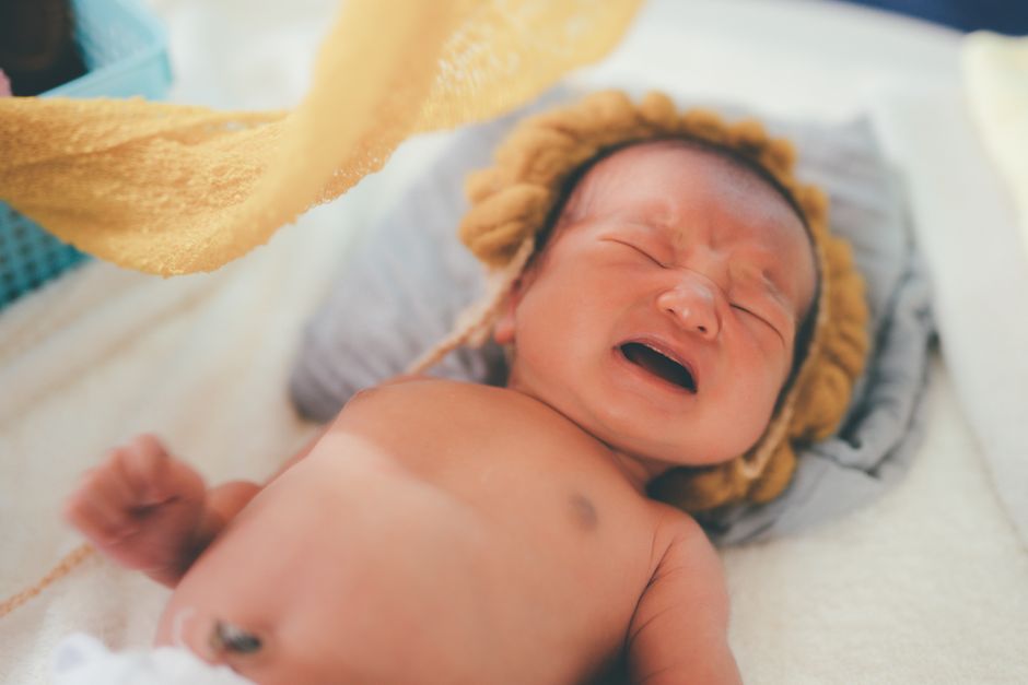Adorable newborn baby wearing a knitted cap, crying while laying on a bed with a soft blanket