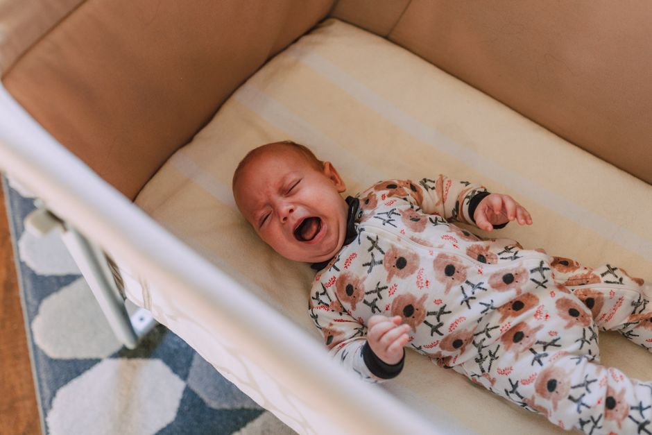 A cute baby in a floral onesie crying in a cozy crib, viewed from above