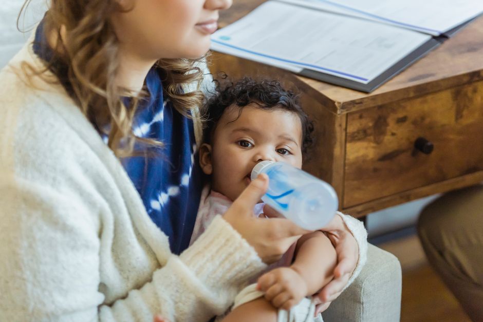 A mother carefully feeding her baby with a bottle while sitting comfortably in a nursery