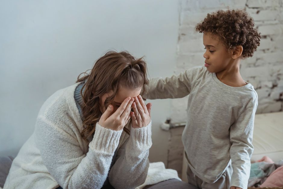 Caring African American son touching shoulder of upset faceless mother covering face