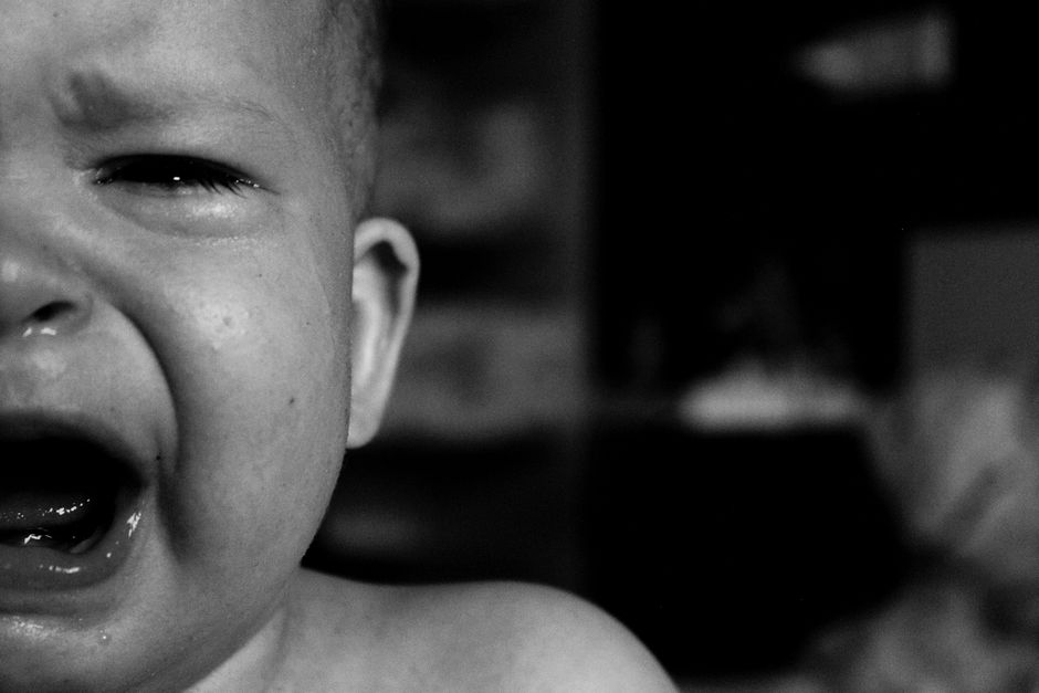 Emotional close-up of a crying baby's face captured in black and white with a blurred background