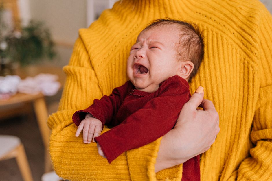 Emotional portrait of a crying newborn being comforted in caregiver's arms indoors